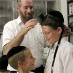 sofer STaM showing a bar mitzvah boy how to put on tefillin, teffilin, phylacteries